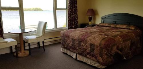 a bedroom with a bed and a table and a window at St Ann's Motel & Cottage in Baddeck