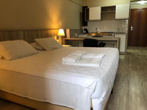 a large white bed in a room with a kitchen at Aquarius Flat Aptos e Suítes in Santa Cruz do Sul