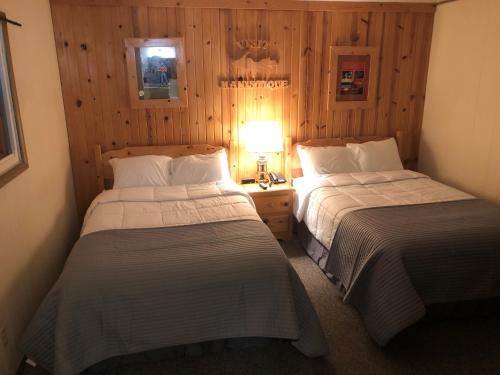 two beds in a room with wooden walls at Holiday Motel in Manistique