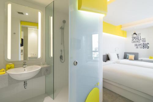 a bathroom with a shower and a sink and a bed at YELLO Hotel Kuta Beachwalk Bali in Kuta
