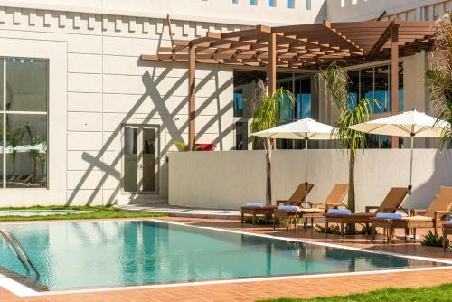 a swimming pool with chairs and umbrellas next to a building at Golden Tulip Zanzibar Airport Hotel & Spa in Zanzibar City