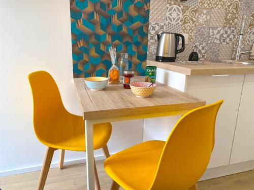 a kitchen with a wooden table and two yellow chairs at Bleu Soleil Rochefort 3 étoiles in Rochefort