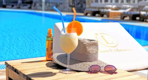 a drink and sunglasses on a table next to a pool at The "L" Suites & Apartments in Argostoli