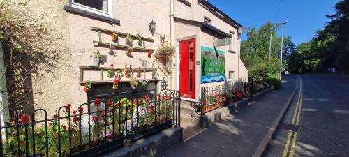 a building with a red door and a fence with flowers at Holly Cottages in Bowness-on-Windermere