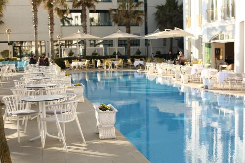a pool with white chairs and tables next to a building at Palace Hotel & SPA in Durrës