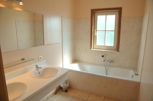 een badkamer met 2 wastafels, een bad en een raam bij Villa Achille in Somme-Leuze