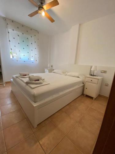 een wit bed in een kamer met een plafondventilator bij espalmador II 7 bajo ALTA TURISTICA in Es Pujols