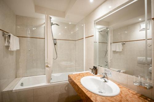 ein Badezimmer mit einem Waschbecken, einer Dusche und einer Badewanne in der Unterkunft Hotel Cristallo in Sulden