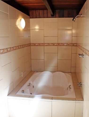 a tub in a bathroom with a tiled wall at Motel Cisne Blumenau (Adult Only) in Blumenau