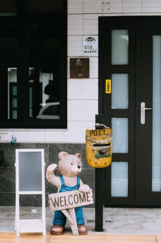 a teddy bear holding a welcome sign in front of a building at 雨禾田 in Sanxing