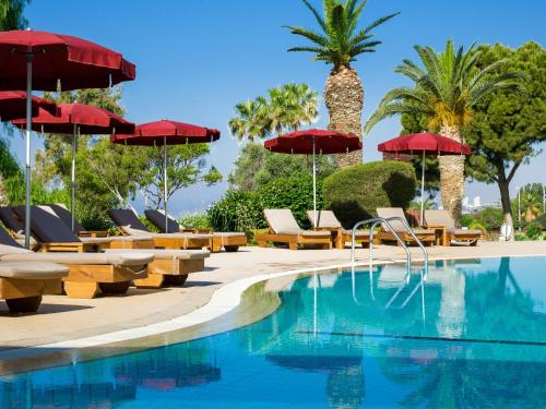 una piscina con sombrillas, sillas y palmeras en St Raphael Resort, en Limassol