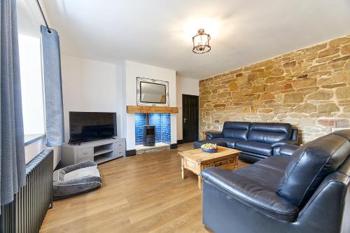 sala de estar con muebles de cuero y pared de piedra. en Host & Stay - Blacksmith's Cottage en Amble