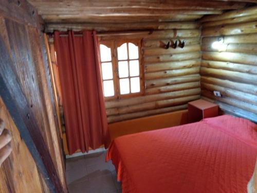 - une chambre avec un lit rouge dans une cabane en rondins dans l'établissement CABAÑAS VALLE LUNLUNTA, à Maipú