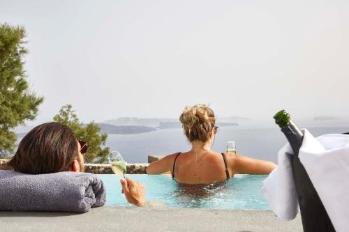 a woman sitting in a swimming pool with a glass of wine at Mr and Mrs White Oia - Santorini in Oia