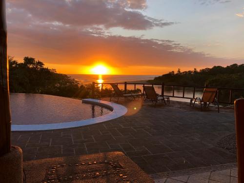 a sunset from a patio with a pool and chairs at Casa Caletas Boutique Hotel in Puerto Coyote