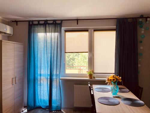 a dining room table with blue curtains and a window at Apartament Wrzos in Dziwnówek