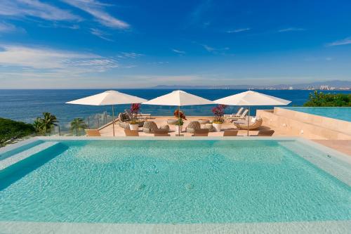 a swimming pool with chairs and umbrellas and the ocean at Maxwell Residences at Indah in Puerto Vallarta
