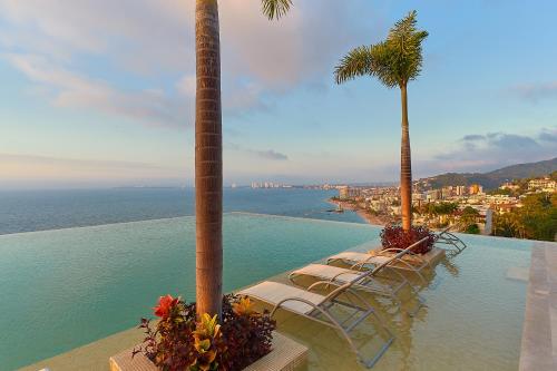 a pool with chairs and palm trees and the ocean at Maxwell Residences at Indah in Puerto Vallarta