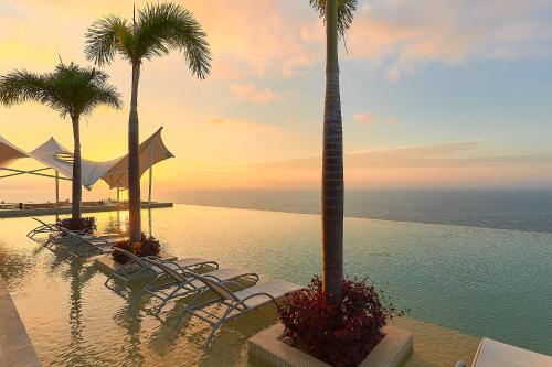 a pool with chairs and palm trees and the ocean at Maxwell Residences at Indah in Puerto Vallarta