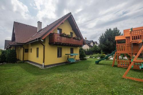 a yellow house with a balcony and a playground at Penzion Rysy in Veľká Lomnica