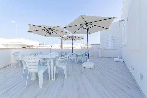 un patio con mesas blancas, sillas y sombrillas blancas en B&B SOLE en Torre San Giovanni Ugento