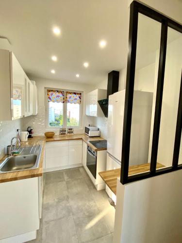 une cuisine avec des armoires blanches, un évier et une fenêtre dans l'établissement Evasion dépaysante en bord de Garonne, à Toulouse