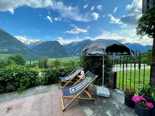 two chairs and an umbrella on a patio with mountains at BergBaur in Neukirchen am Großvenediger