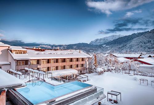 a building with a snow covered roof with a pool at Obermühle 4*S Boutique Resort in Garmisch-Partenkirchen