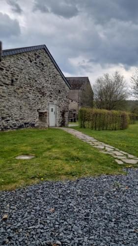a stone building with a white door and a grass yard at Le Maissin 1876 in Paliseul