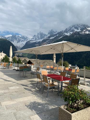 a patio with tables and chairs with mountains in the background at Hotel La Soglina in Soglio