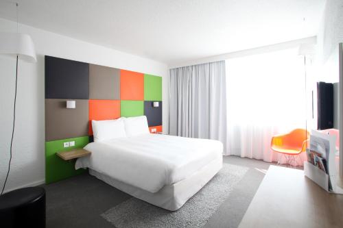 a bedroom with a white bed and a colorful wall at ibis Styles Nancy Sud in Houdemont