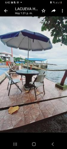 a picnic table with a blue umbrella and chairs at Hotel la Cueva Limon in Puerto Limón