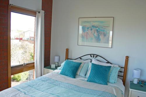 a bedroom with a bed with blue pillows and a window at Garland Grove in Ocean Grove