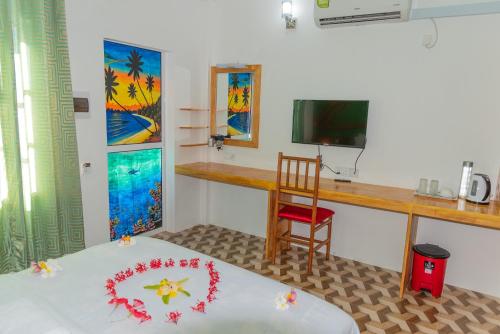 a room with a bed and a desk and a television at Chao Guest House in Maafushi