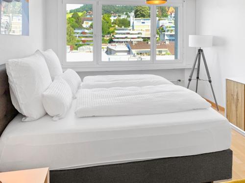 1 cama con sábanas blancas y almohadas en una habitación en ARISER - Mountain View Business Apartment, en Zug