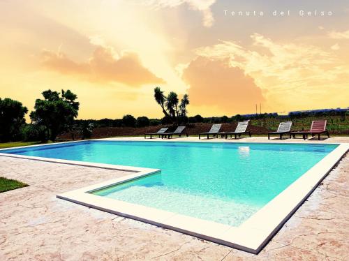 a swimming pool with chairs and a sunset in the background at Tenuta del Gelso in Catania