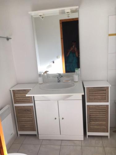 ein Badezimmer mit einem Waschbecken und einer Person im Spiegel in der Unterkunft Odalys , hauts de Salavas in Salavas