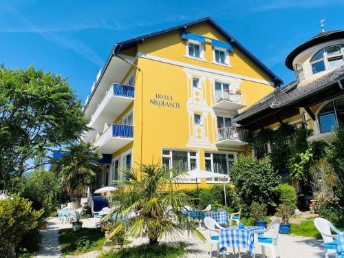 ein gelbes Hotel mit Tischen und Stühlen davor in der Unterkunft Hotel Nikolasch in Millstatt