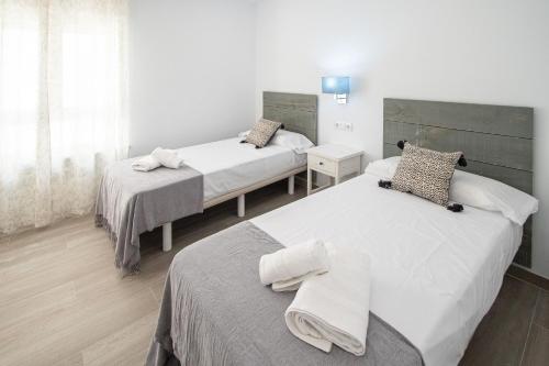 two beds in a bedroom with white walls and wood floors at Nuevo Mirandilla Apartment - Cadiz Beach in Cádiz