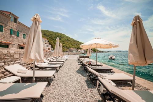 a row of beach chairs with umbrellas and the water at Apartments Villa Jelena in Tivat
