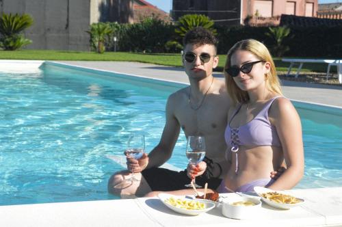 a man and woman sitting next to a pool with wine glasses at Mauro Home Bed and Relax in Linguaglossa
