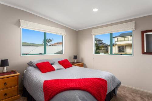 a bedroom with a bed with red pillows and two windows at Ohope Palms - Ohope Holiday Home in Ohope Beach