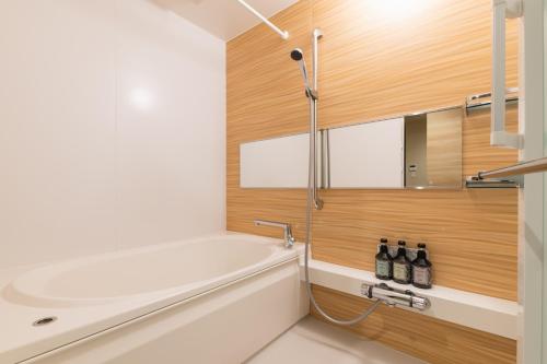 a bathroom with a white tub and a wooden wall at GRAND BASE Saiwaimachi in Nagasaki