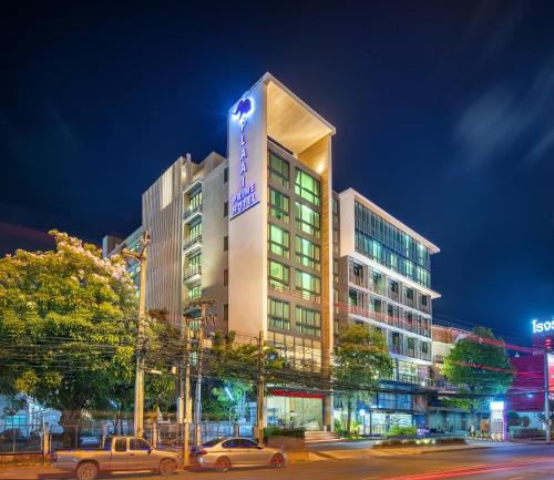 Un grand bâtiment avec des voitures garées devant lui dans l'établissement PLAAI Prime Hotel Rayong SHA Extra Plus, à Rayong