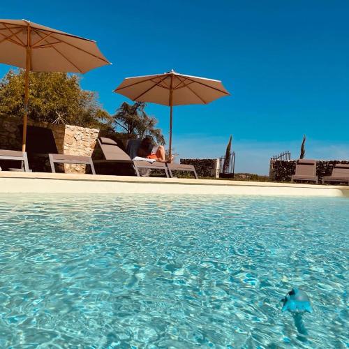 une piscine d'eau avec 2 personnes assises sous des parasols dans l'établissement Chez Brunet chambres d'hôtes et gîte, à Gondrin