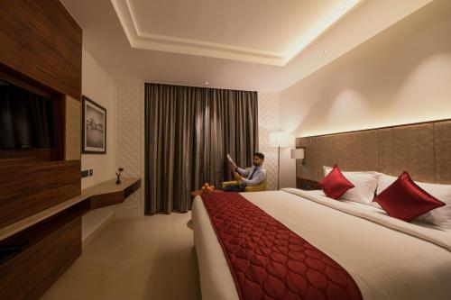 a man sitting on a bed in a hotel room at AARYA MANSION V One Hotel in Hassan