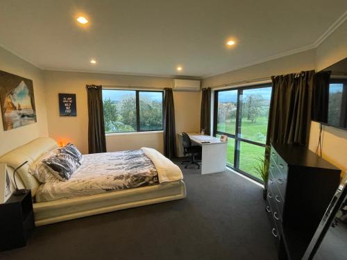 a bedroom with a bed and a desk and windows at Paraite Farmstay in New Plymouth