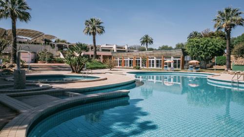 une piscine bordée de palmiers et un bâtiment dans l'établissement MClub Alicudi, à Sciacca