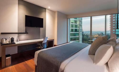 a hotel room with a bed and a desk with a television at NH Collection Guadalajara Providencia in Guadalajara