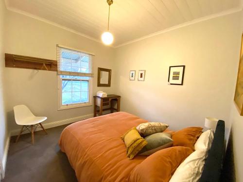 a bedroom with a bed and a chair and a window at Loose Leaf Cottage in Kyneton
